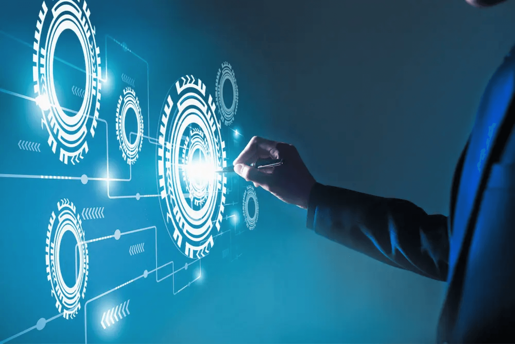 A hand holding a pen to a glowing diagram of interlocking gears on a blue screen.